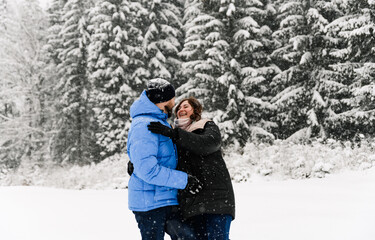 Fototapeta na wymiar Walk in winter. Embracing couple enjoying snowfall. Man and woman having fun in the frosty forest. Romantic date in winter time.Christmas mood of a young family. Love and leisure concept