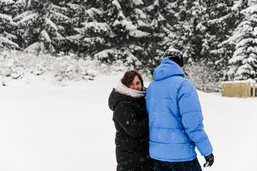 Walk in winter. Embracing couple enjoying snowfall. Man and woman having fun in the frosty forest. Romantic date in winter time.Christmas mood of a young family.  Love and leisure concept