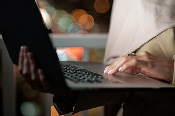 Hand of young businesswoman touching panel by laptop keypad while networking at night time