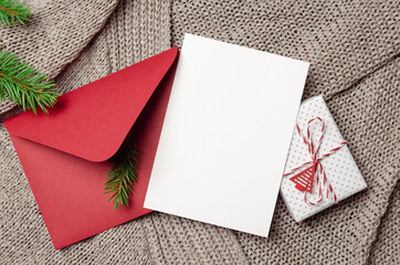 Christmas greeting card mockup with decorated gift box, red envelope and fir tree branches