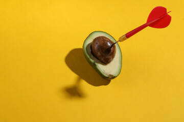Avocado with darts on a yellow background. Minimal layout