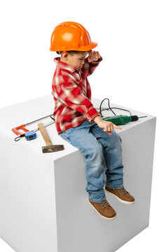 Cute little preschool boy, kid in image of builder, architect in orange protective helmet sitting on huge box isolated on white background