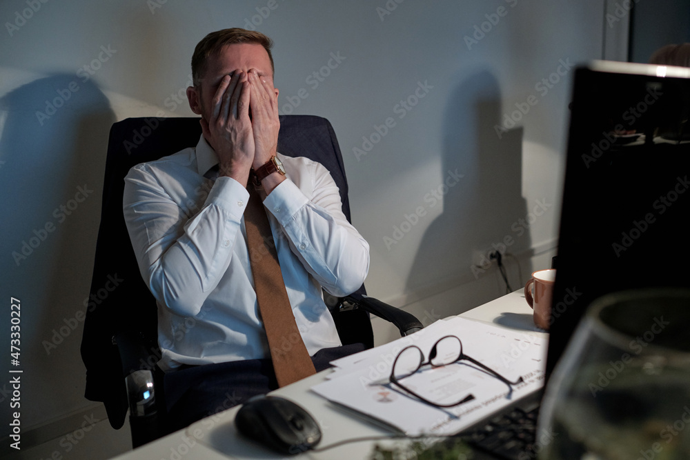 Aufkleber exhausted businessman covering his face by hands while sitting in front of computer by workplace in 