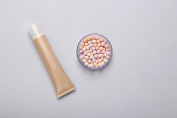 Fototapeta na wymiar Tube of foundation and balls of powder on gray background. Cosmetics. Top view