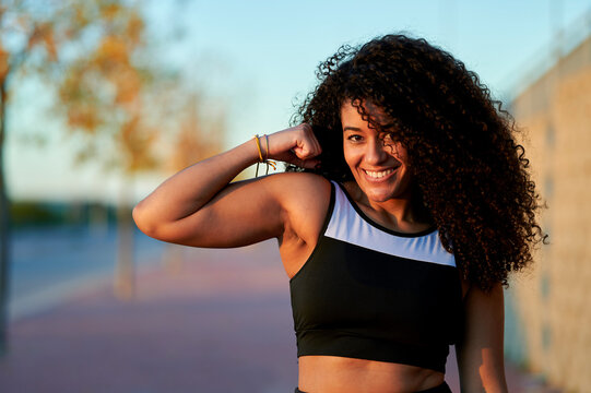 Smiling sportswoman flexing muscles at sunset