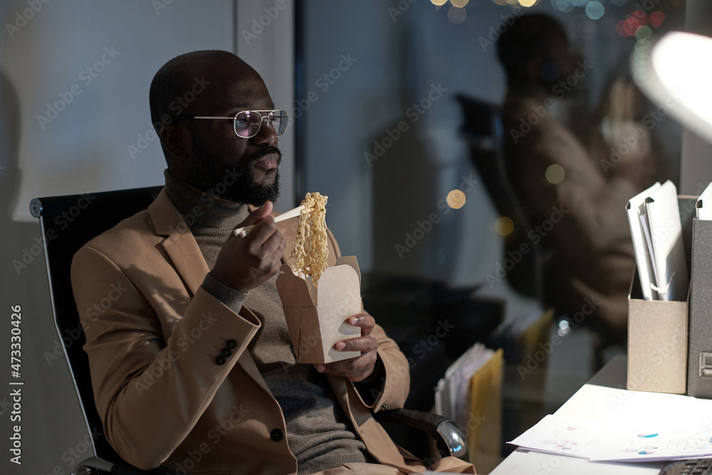Aufkleber young serious businessman eating wok in front of computer while working overtime in office at night