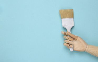 Wooden hand holding paintbrush on blue pastel background. Copy space
