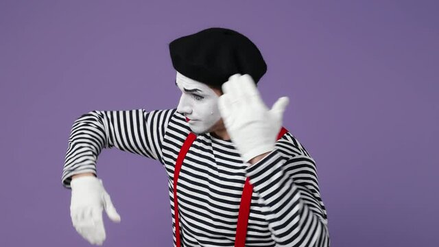 Charismatic stunning marvelous young mime man with white face mask wears striped shirt beret playing puppet role showing pantomime isolated on plain pastel light violet background studio portrait