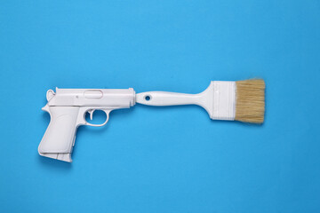 White gun with paint brush on blue background. Minimal, creative layout, top view