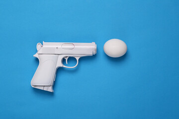 White gun with egg on a blue background. Minimal, creative layout, say no war