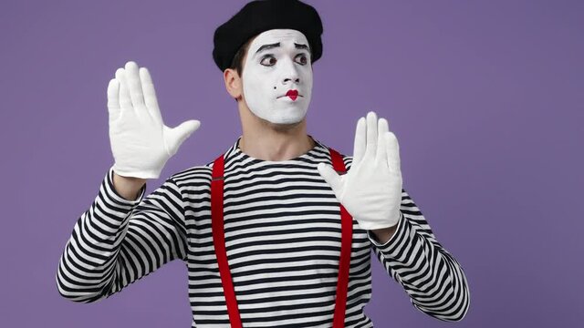 Charismatic stunning marvelous magnificent happy young mime man with white face mask wears striped shirt beret perform invisible wall isolated on plain pastel light violet background studio portrait