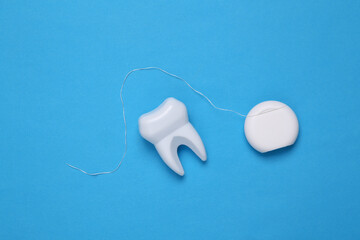 Dental care concept. Plastic tooth with dental floss on blue background