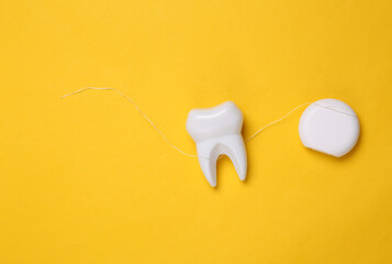 Dental care concept. Plastic tooth with dental floss on yellow background
