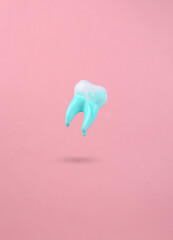Levitating tooth with dripping turquoise paint on a pink background. Minimal creative layout. Concept art.