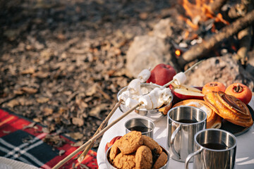 Autumn picnic in the forest. Thermos and metal tourist mugs with tea, fruits, buns and cookies.