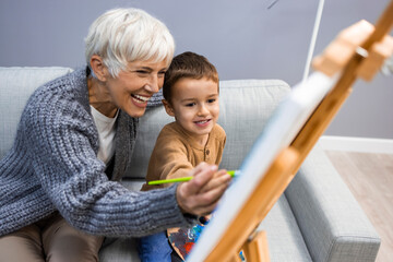 Grandson and grandma painting on canvas. Artist teaching young boy how to paint at home. Happy...