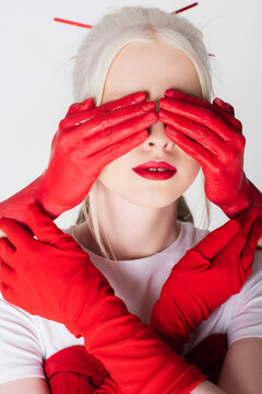 Female hands in red paint covering eyes of albino model isolated on white.