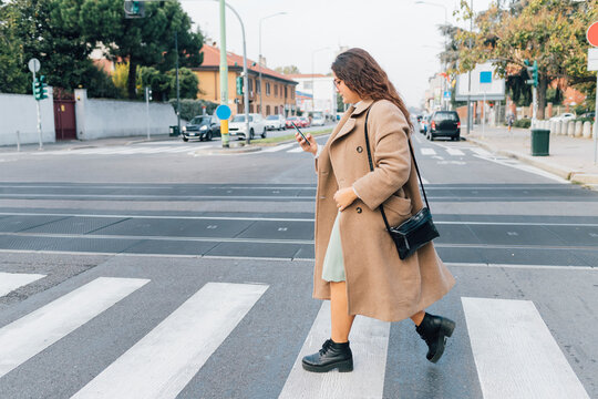 Plus size woman using smart phone while crossing road