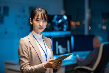 Young serious female programmer or developer in formalwear holding tablet while networking in office environment