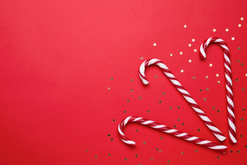 Delicious Christmas candy canes and confetti on red background, flat lay. Space for text