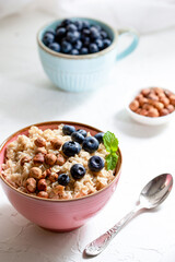 Herculean porridge with hazelnuts, granola and blueberries in a pink plate o white table. 