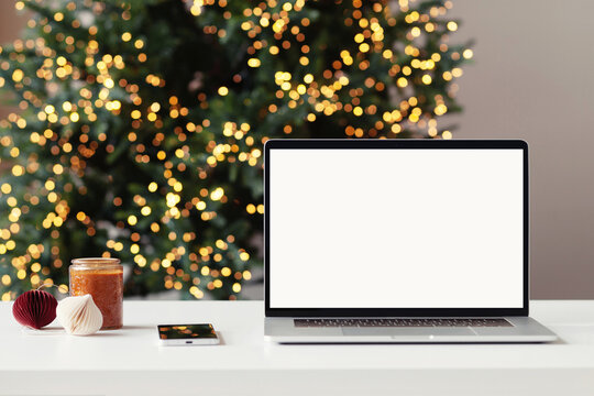 Work place during Christmas holidays, laptop computer with blank white mockup screen. Online shopping during winter holiday, ordering xmas gifts concept. Website template