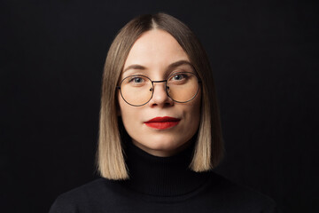 Close up woman portrait wearing glasses with black frames, with red lips on black background with positive focused face expression