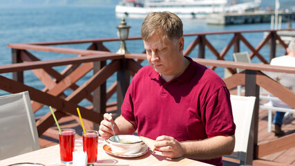 An adult blonde man has lunch on beach in a cafe in the fresh air. © ALEXEY
