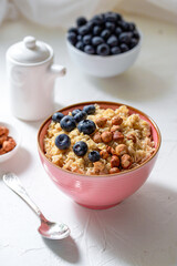 Herculean porridge with hazelnuts, granola and blueberries in a pink plate o white table. 