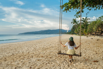 Lonely woman tourist sitting on a swing on a white sand beach by the sea