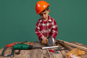 Portrait of cute little boy, kid in image of builder, designer in orange protective helmet using...
