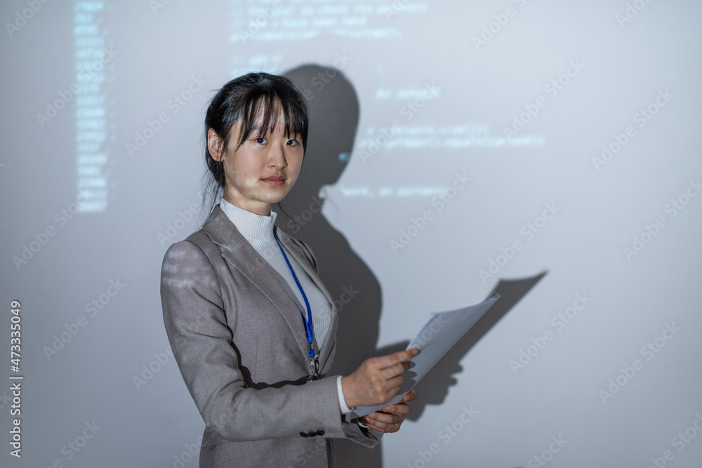 Poster young confident coach with paper standing by interactive whiteboard and looking at you during presen