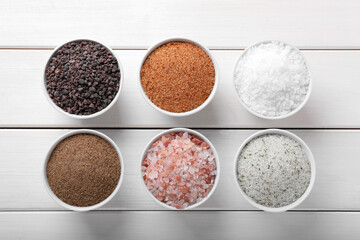 Different kinds of salt on white wooden table, flat lay