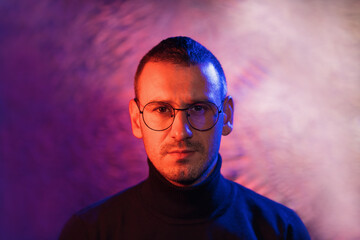 Neon portrait of serious man wearing glasses with black frame and dark turtleneck sweater on cosmic silver multicolored background