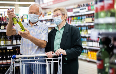 mature european spouses chooses bottle of wine in alcohol section of supermarket