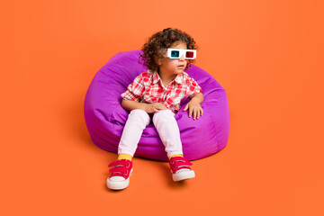 Photo of adorable impressed schoolgirl wear plaid outfit 3d glasses sitting bean bag isolated orange color background