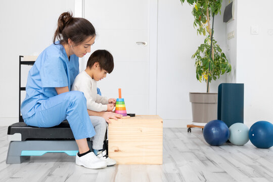 Therapist doing development activities with a little boy with cerebral palsy, having rehabilitation, learning . Training in medical care center. High quality photo.