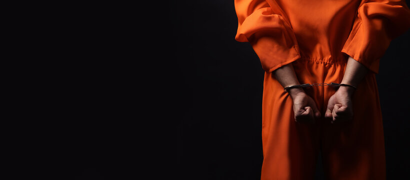 Prisoner in jumpsuit with handcuffs on black background, closeup. Space for text