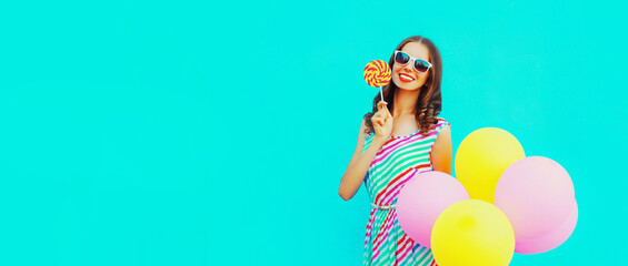 Portrait of cheerful happy smiling young woman with bunch of colorful balloons and lollipop on blue background