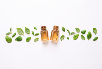 Bottles of essential basil oil and fresh leaves on white background, flat lay