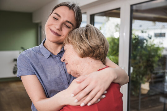 Smiling caregiver hugging senior woman at home