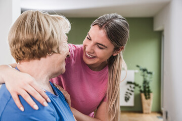Young physiotherapist with hand on woman's shoulder at home
