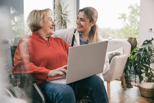 Disabled woman with laptop looking at nurse by wheelchair