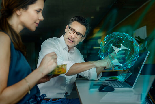Businessman explaining augmented hologram to colleague in office