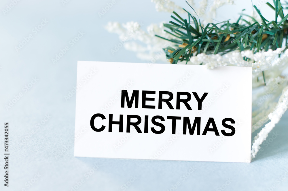 Poster card with the text merry christmas on a light background next to a branch of a spruce tree