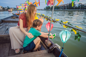 Happy family Mother and son of travelers ride a national boat on background of Hoi An ancient town,...