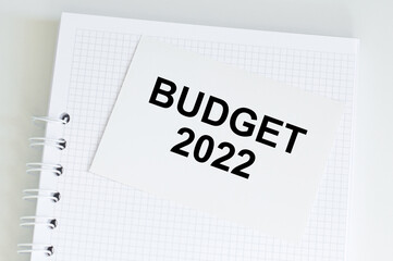 Text BUDGET 2022 on card, which lies on a white notebook on a light table