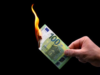 male hand holds a burning 100 euro banknote isolated on black background, concept image of inflation