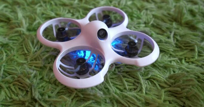 small indoor home brushless fpv quadcopter lies on green carpet and flies away and shines with neon colorful lights 