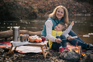 Mom and daughter fries marshmallows on sticks by the fire.